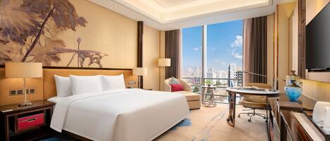 A hotel room with a large bed, a desk, a chair, a TV, and a city view.