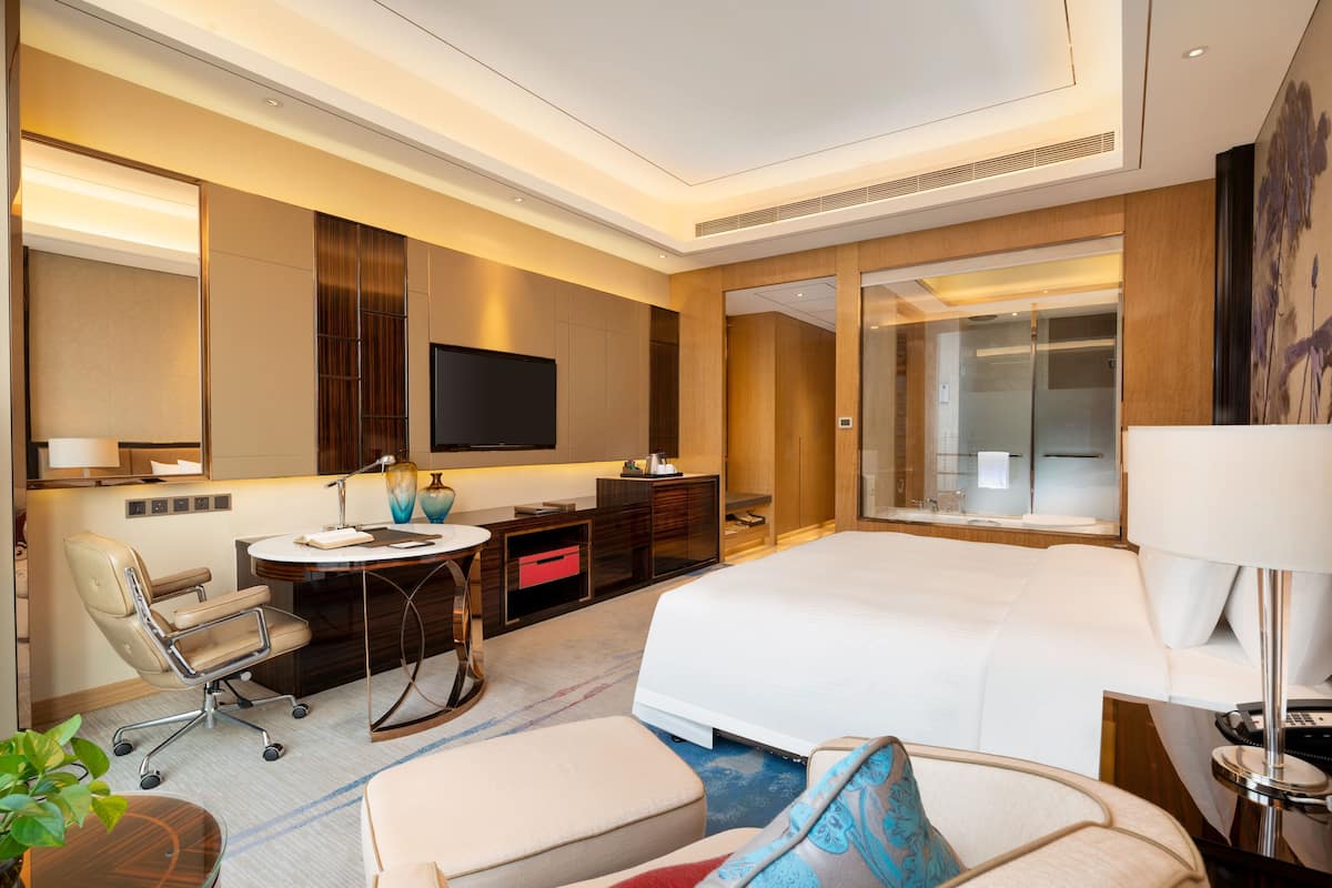 Een moderne hotelkamer met een groot bed, een bureau met stoel, een televisie en een klein tafeltje met lamp.