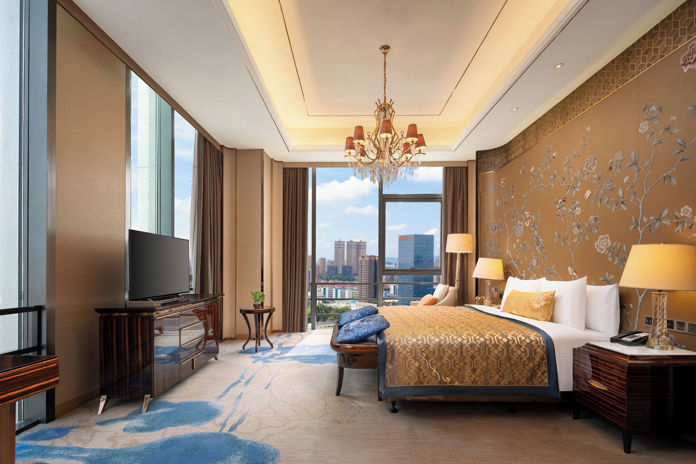 Ein Hotelzimmer mit einem großen Bett, einem Fernseher, einer Kristallleuchtre und Blick auf die Stadt.