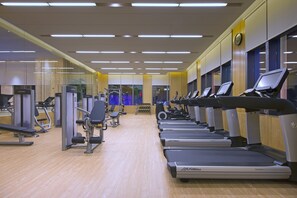 Un gimnasio con cintas de correr, máquinas de pesas y un espejo grande.