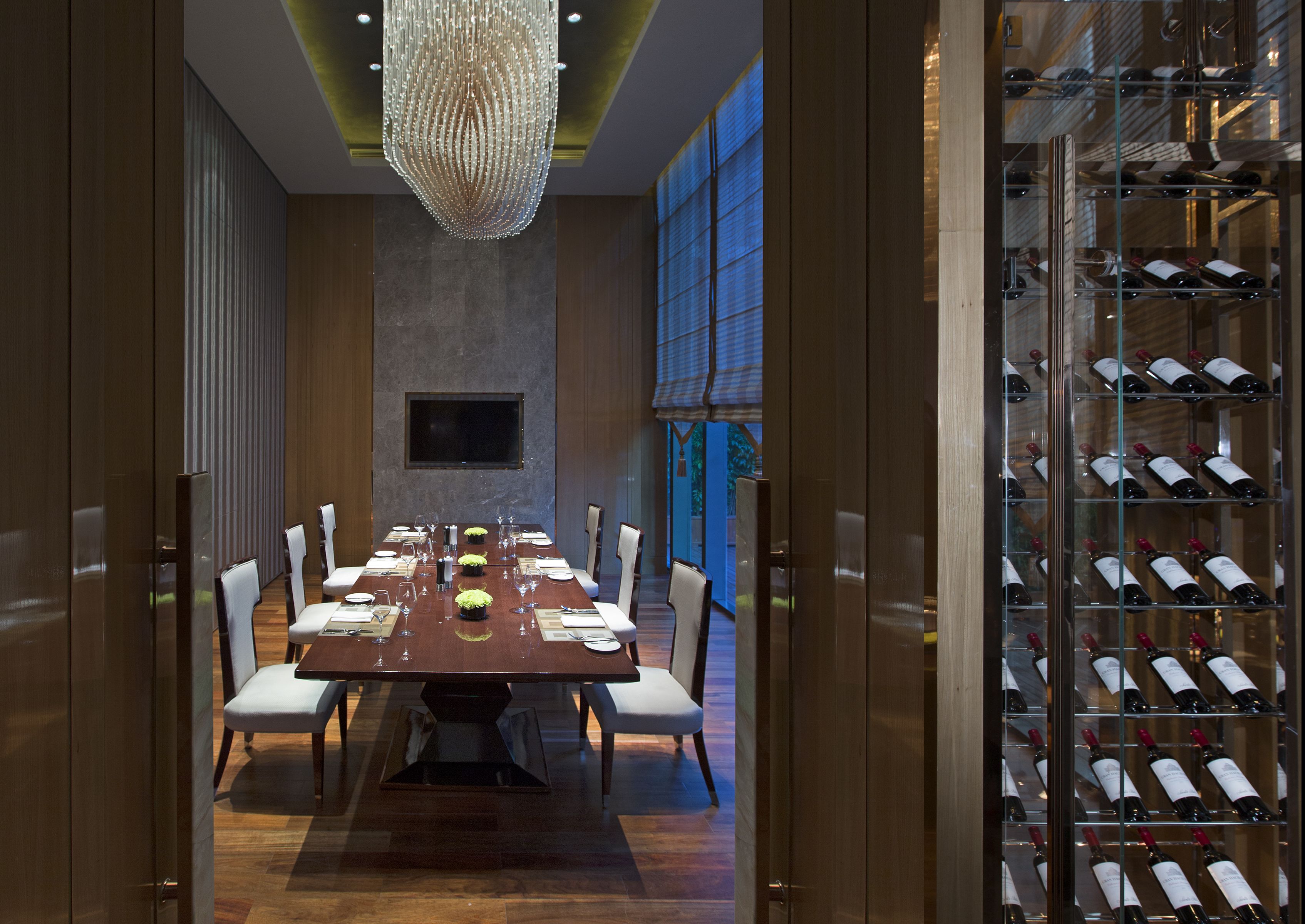 Ein formeller Speisesaal mit einem langen Tisch, der für eine Mahlzeit gedeckt ist, einem Weinkühlschrank mit mehreren Flaschen und einer großen Chandelier.