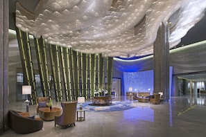 A spacious lobby with a modern design, featuring a central seating area, a reception desk, and a decorative ceiling.
