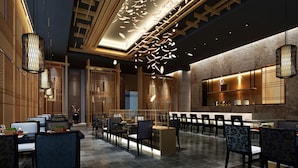Un hall d’hôtel moderne doté d’un espace salon central, d’un comptoir d’accueil et d’un bar avec un mur en pierre en arrière-plan.