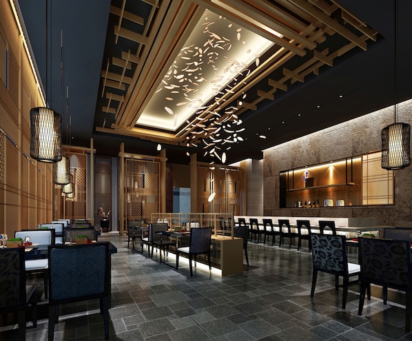 A modern hotel lobby with a central seating area, a reception desk, and a bar area with a stone wall backdrop.