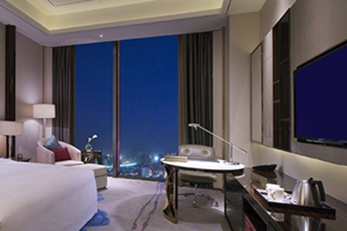Een hotelkamer met een groot bed, een bureau, een stoel, een kleine tafel en een groot raam met uitzicht op de stad.
