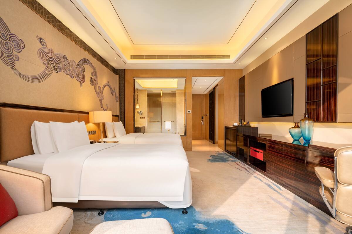 Een hotelkamer met een groot bed, een bureau, een televisie en een decoratief muurschildering.