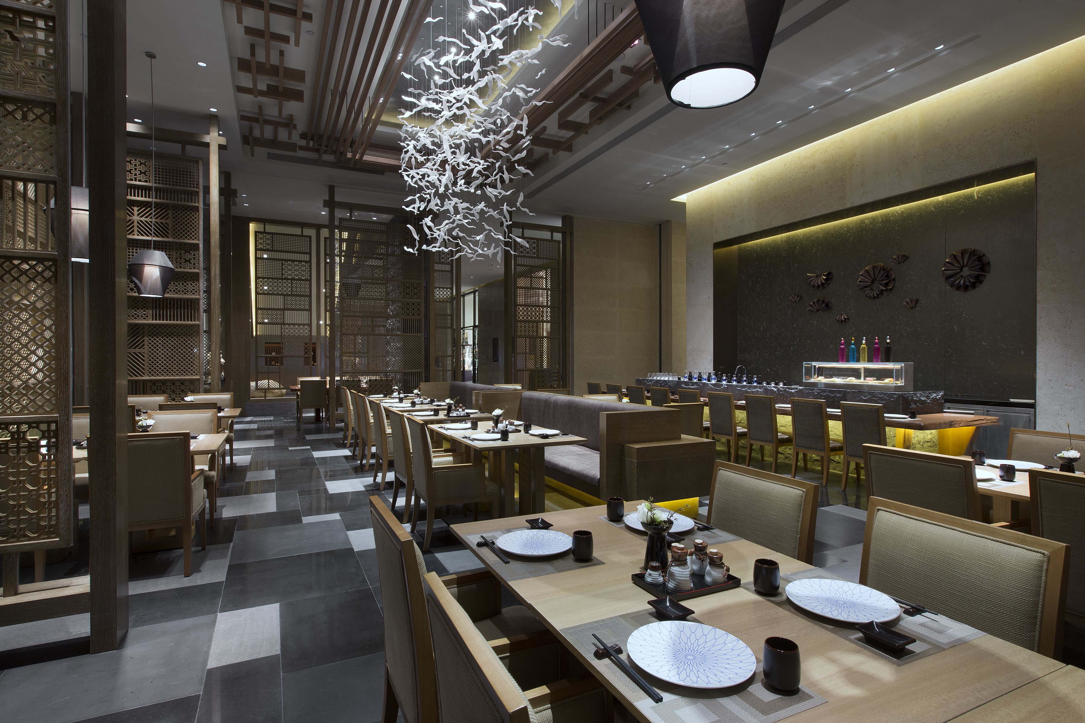 Un restaurante moderno con mesas compartidas largas, sillas de madera y una lámpara decorativa en el techo.