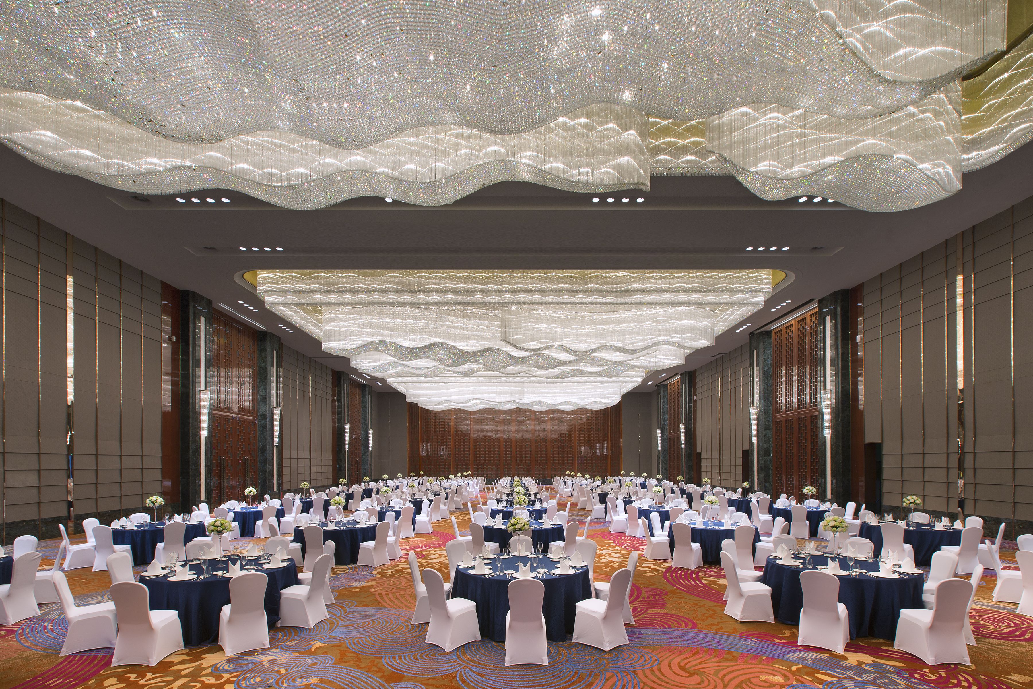 A large banquet hall with round tables set for events, white chairs, and a decorative ceiling.