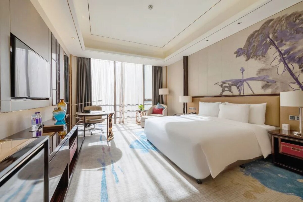 Een hotelkamer met een groot bed, een bureau, een stoel, een televisie en een schilderij aan de muur.