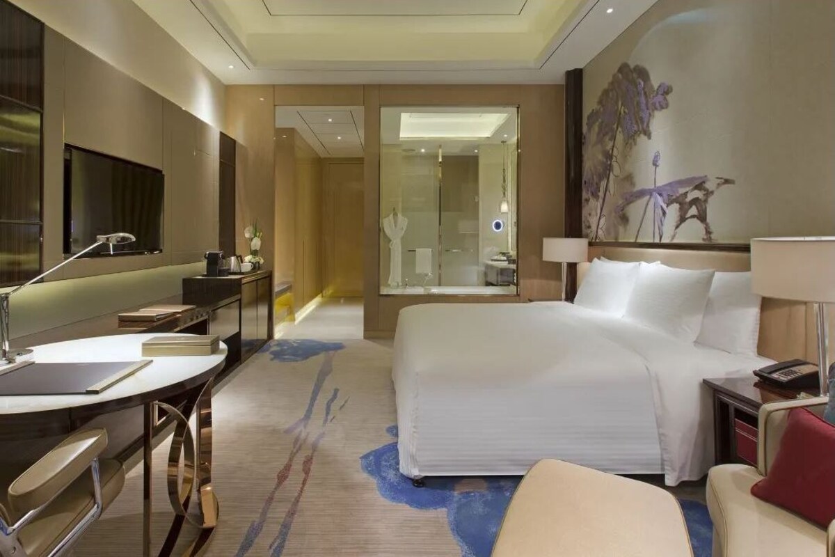 Habitación de hotel con cama, escritorio, silla y un espejo grande.
