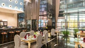 A modern restaurant interior with high ceilings, large windows, and a variety of seating arrangements including tables and chairs. - Sea Me Spring Too Hotel (Pattaya)
