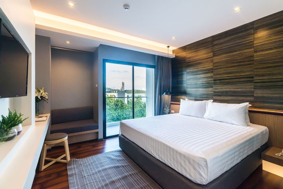 A modern hotel room with a large bed, a desk, a chair, and a view of the city.
