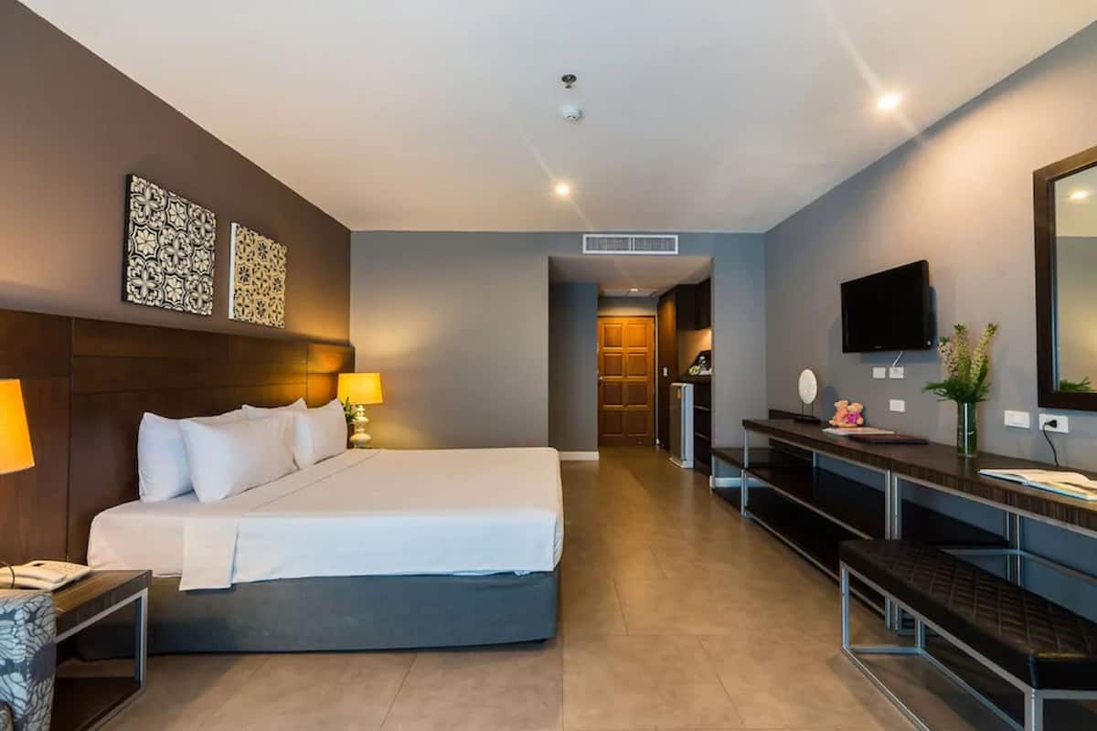 A modern hotel room with a large bed, bedside table, lamp, and a TV mounted on the wall.