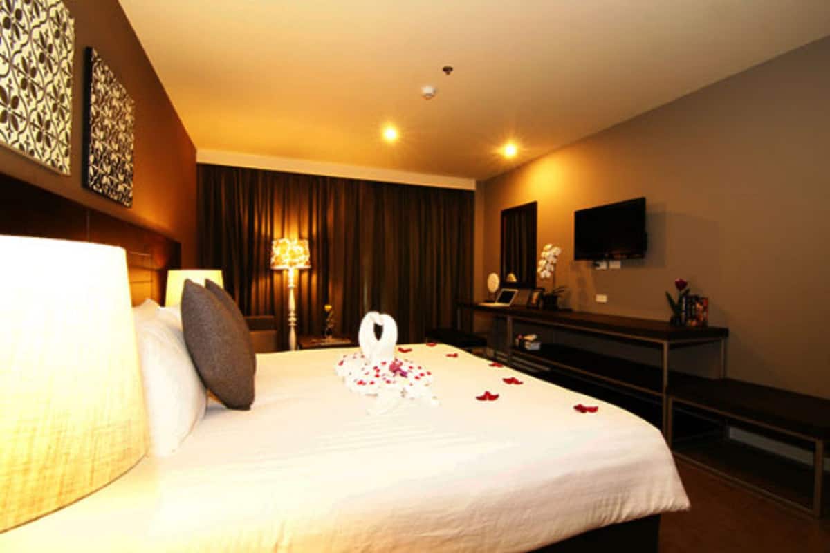 A hotel room with a large bed, a desk, a flat-screen TV, and a large window with curtains.