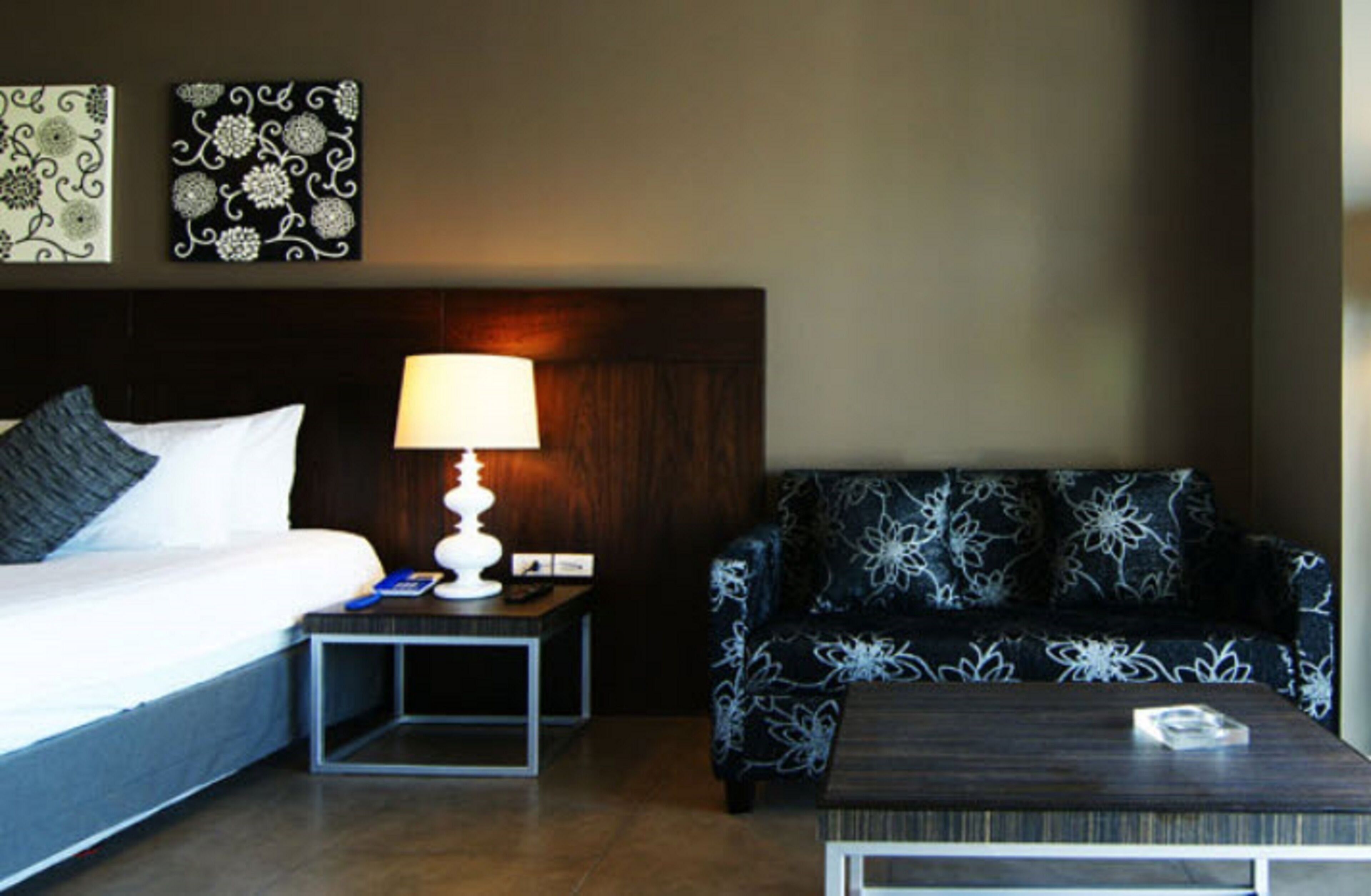 Ein Hotelzimmer mit Bett, Nachttisch mit Lampe, Sofa und Couchtisch.