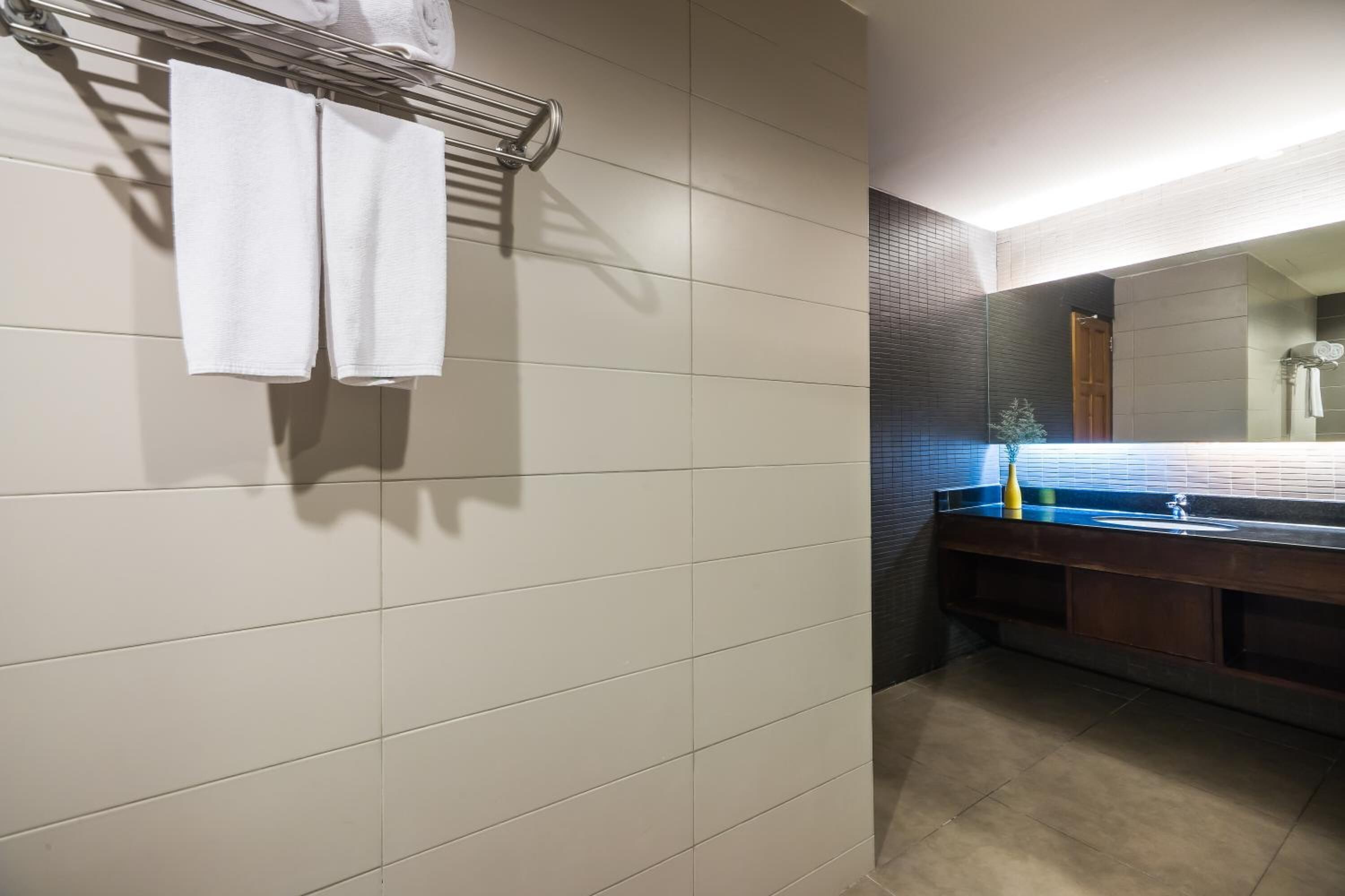 Une salle de bain avec un mur carrelé, un porte-serviettes avec deux serviettes, un lavabo avec un miroir et un espace douche.