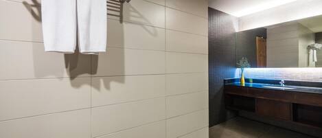 Une salle de bain avec un mur carrelé, un porte-serviettes avec deux serviettes, un lavabo avec un miroir et un espace douche.