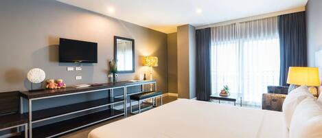 Une chambre d’hôtel dotée d’un grand lit, d’un téléviseur à écran plat fixé au mur, d’un bureau avec une lampe et d’une fenêtre avec des rideaux.