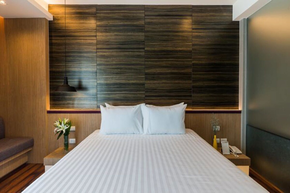 A hotel room with a large bed, a nightstand with a lamp, and a wall-mounted artwork.