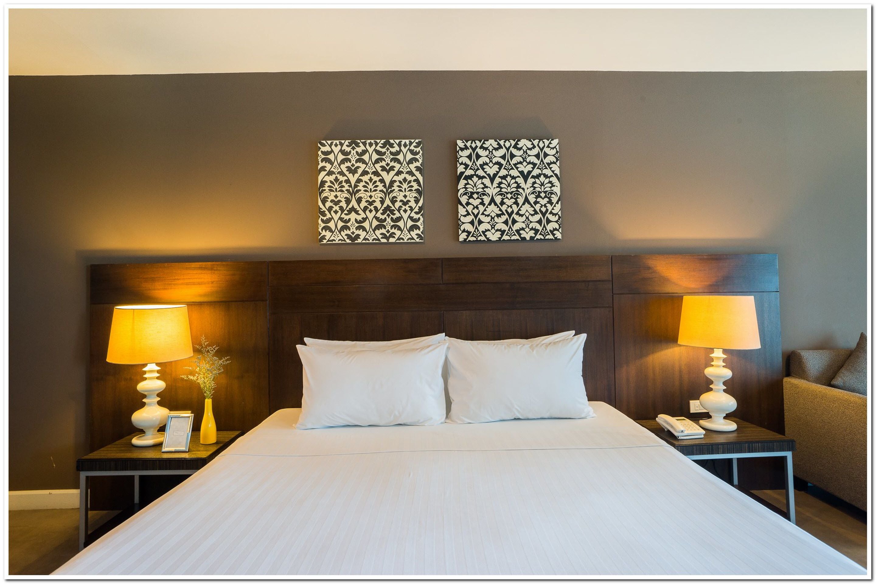 A neatly made bed with two pillows, a wooden headboard, two bedside tables with lamps, and two wall-mounted decorative panels.