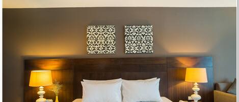 A neatly made bed with two pillows, a wooden headboard, two bedside tables with lamps, and two wall-mounted decorative panels.
