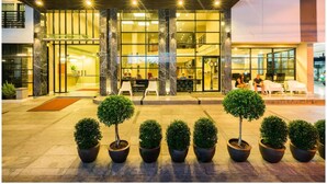 A modern hotel entrance with a glass facade, marble columns, and potted topiary plants. - Sea Me Spring Hotel (Pattaya)