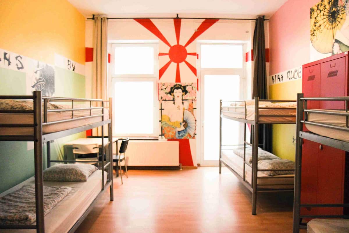 Un dormitorio con literas, un radiador y un ventanal con diseño de sol.