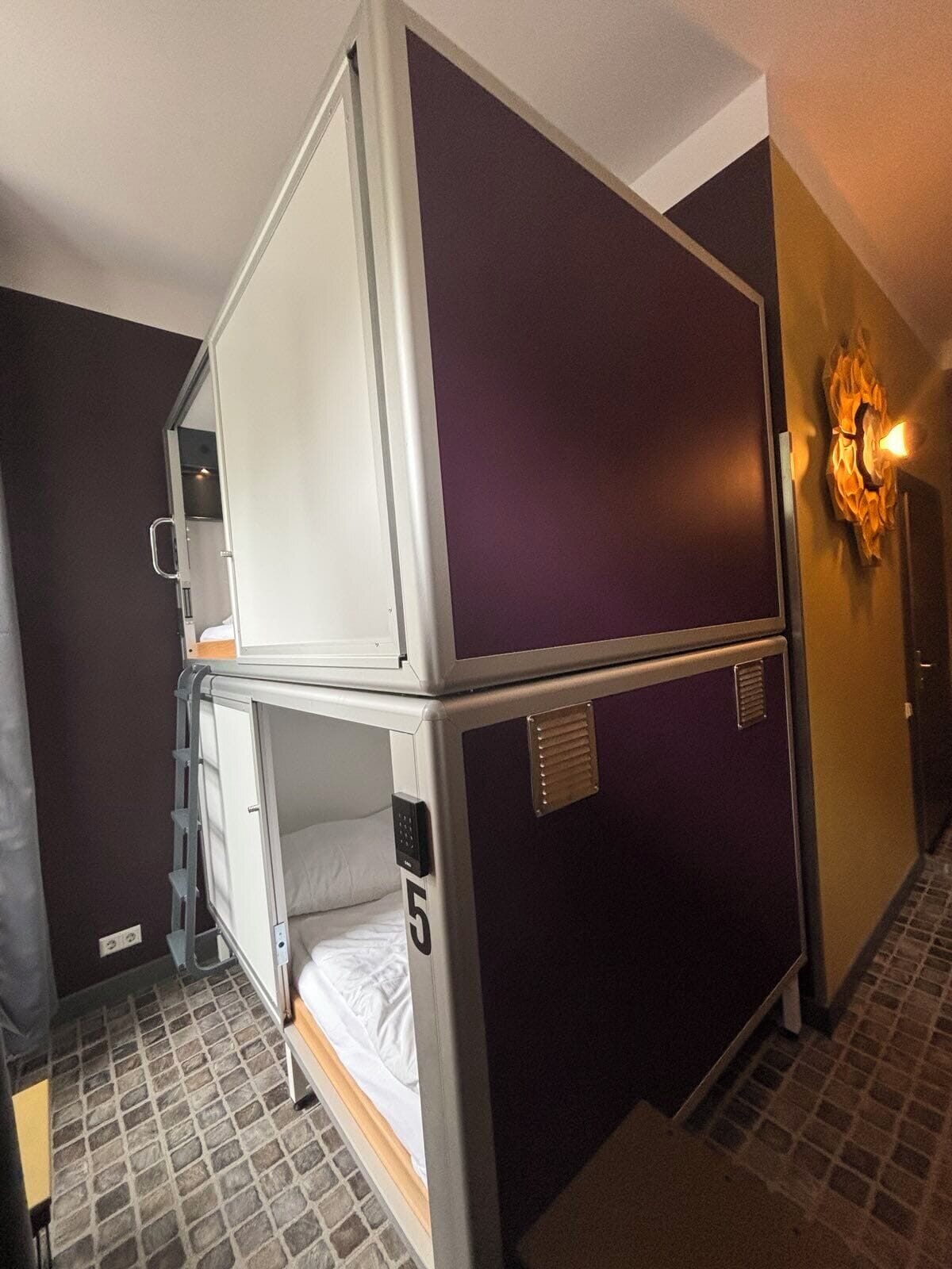 A bunk bed room with a small desk and a wall-mounted light fixture.
