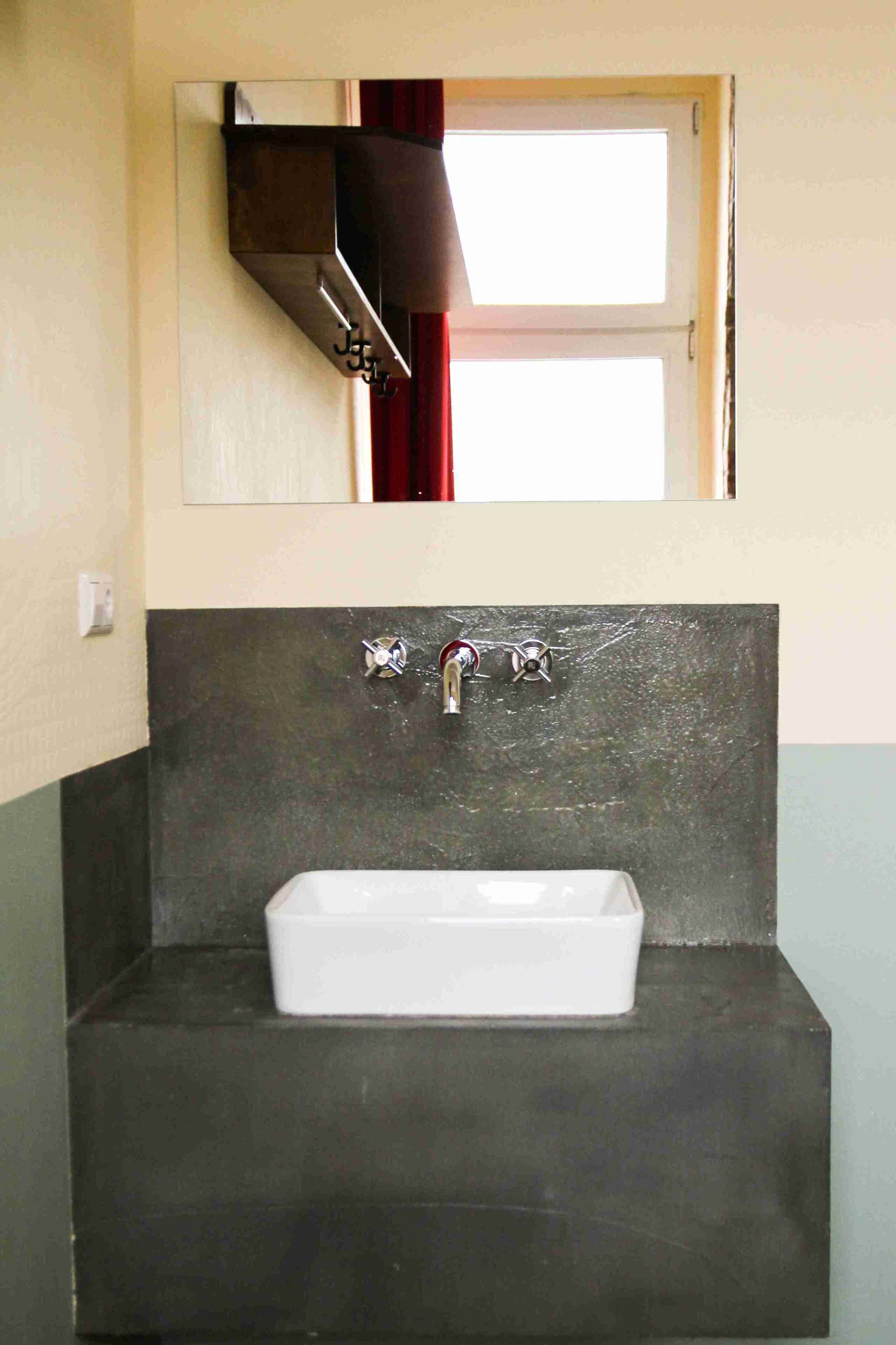 A bathroom with a rectangular sink, a mirror above it, and a window with red curtains.