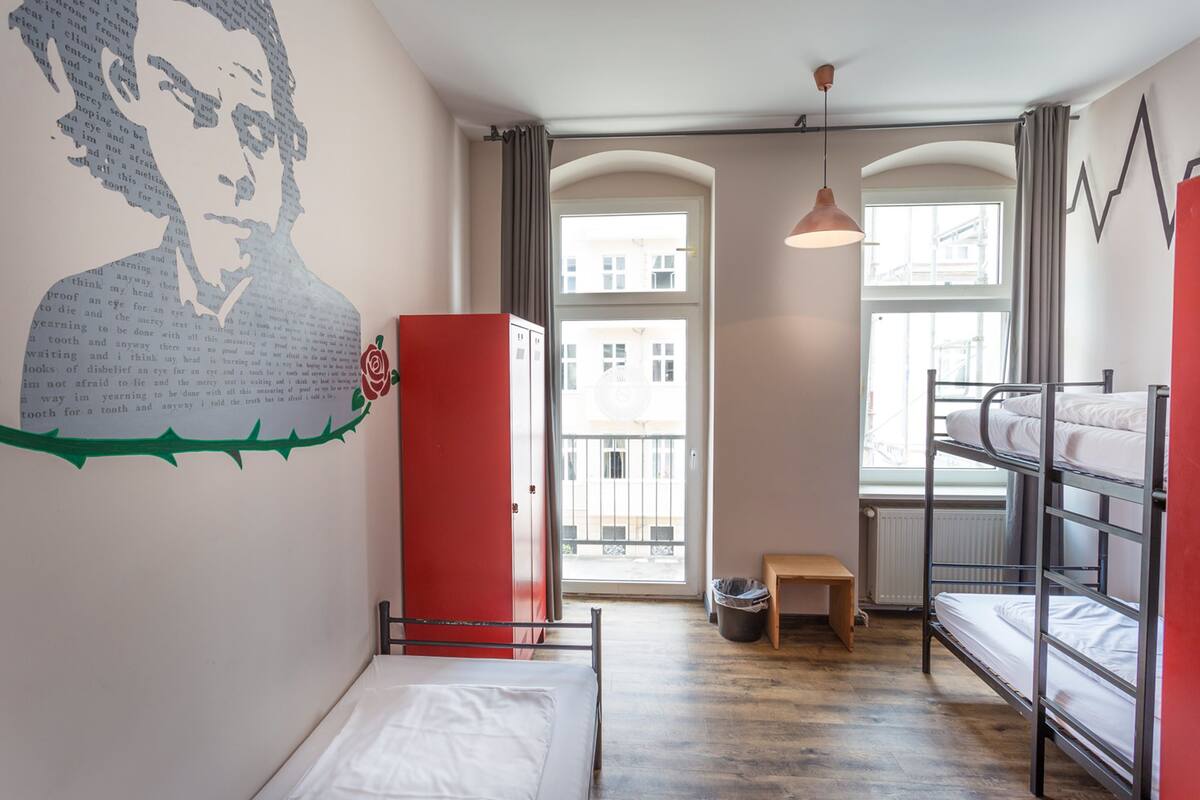 Un dormitorio con literas, un armario rojo, un mural en la pared y vistas a edificios a través de la ventana.