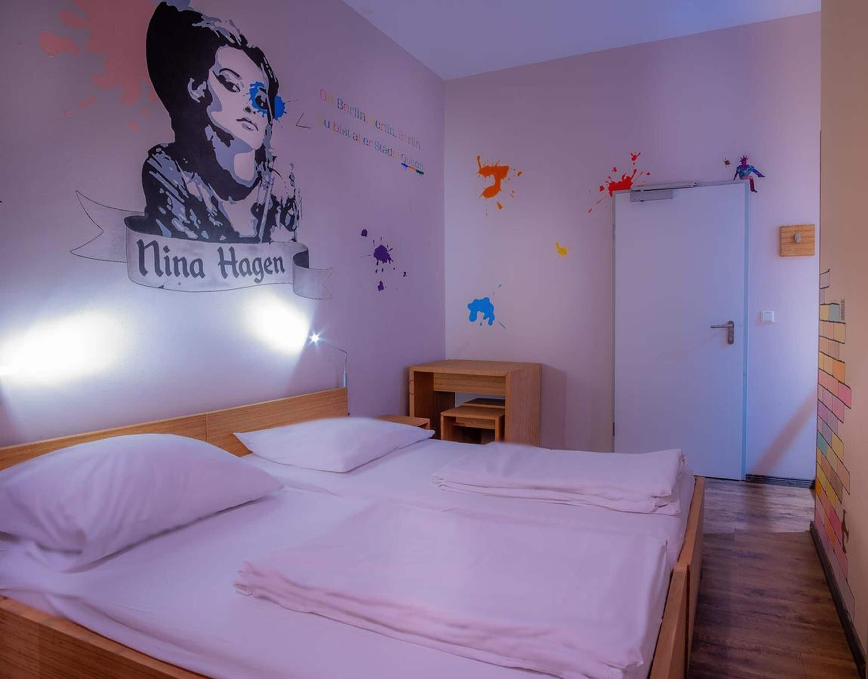 A bedroom with a bed, a nightstand, a wall with a poster, and a door.