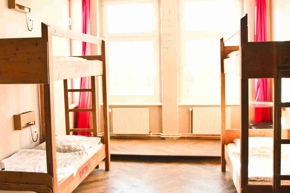 Un dormitorio con literas, pisos de madera y ventanas amplias con cortinas rojas.