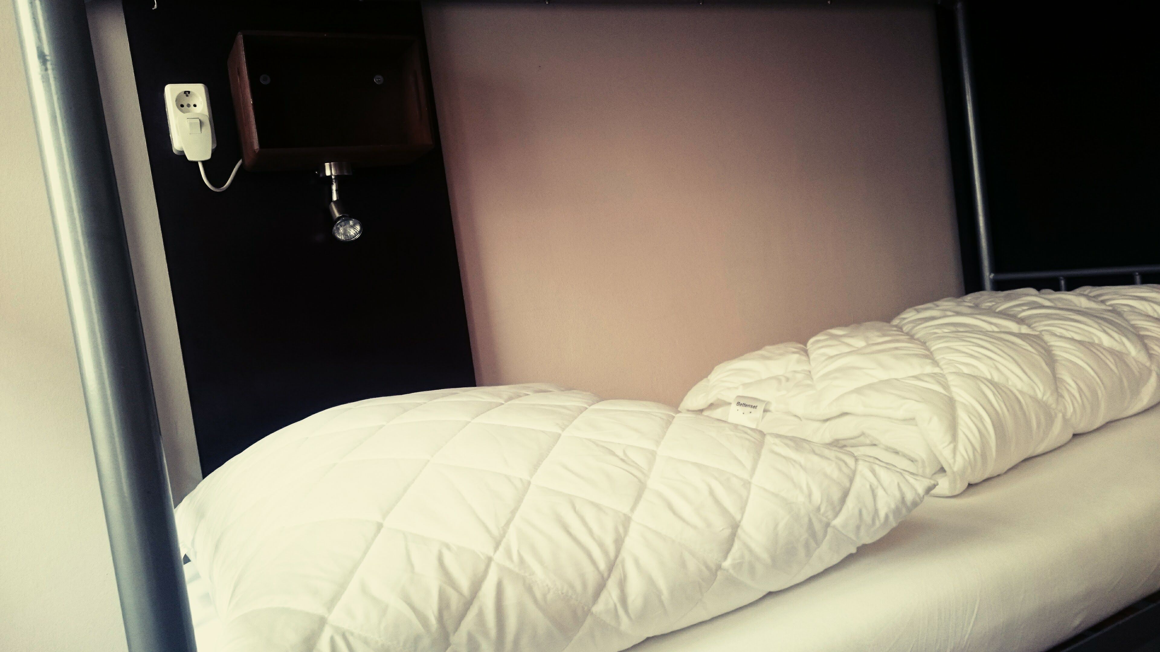 Un lit simple avec une couette blanche matelassée, dans une chambre avec des lits superposés.