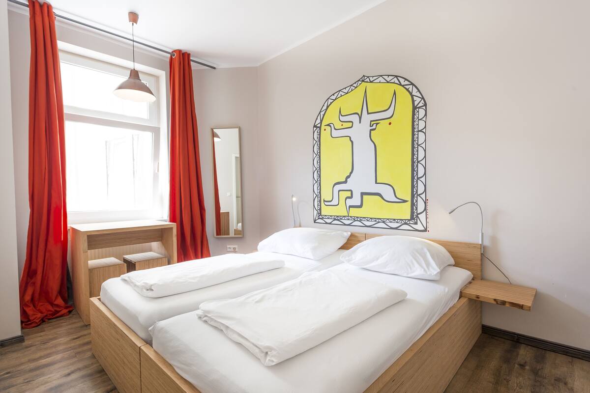 Una habitación de hotel moderna con una cama de madera, ropa de cama blanca, un escritorio y un espejo grande.