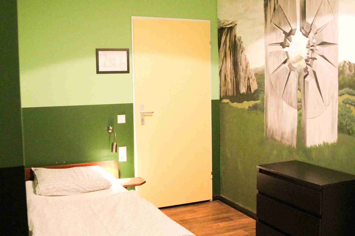Un dormitorio con cama, cómoda, pared verde y una lámpara en el techo.