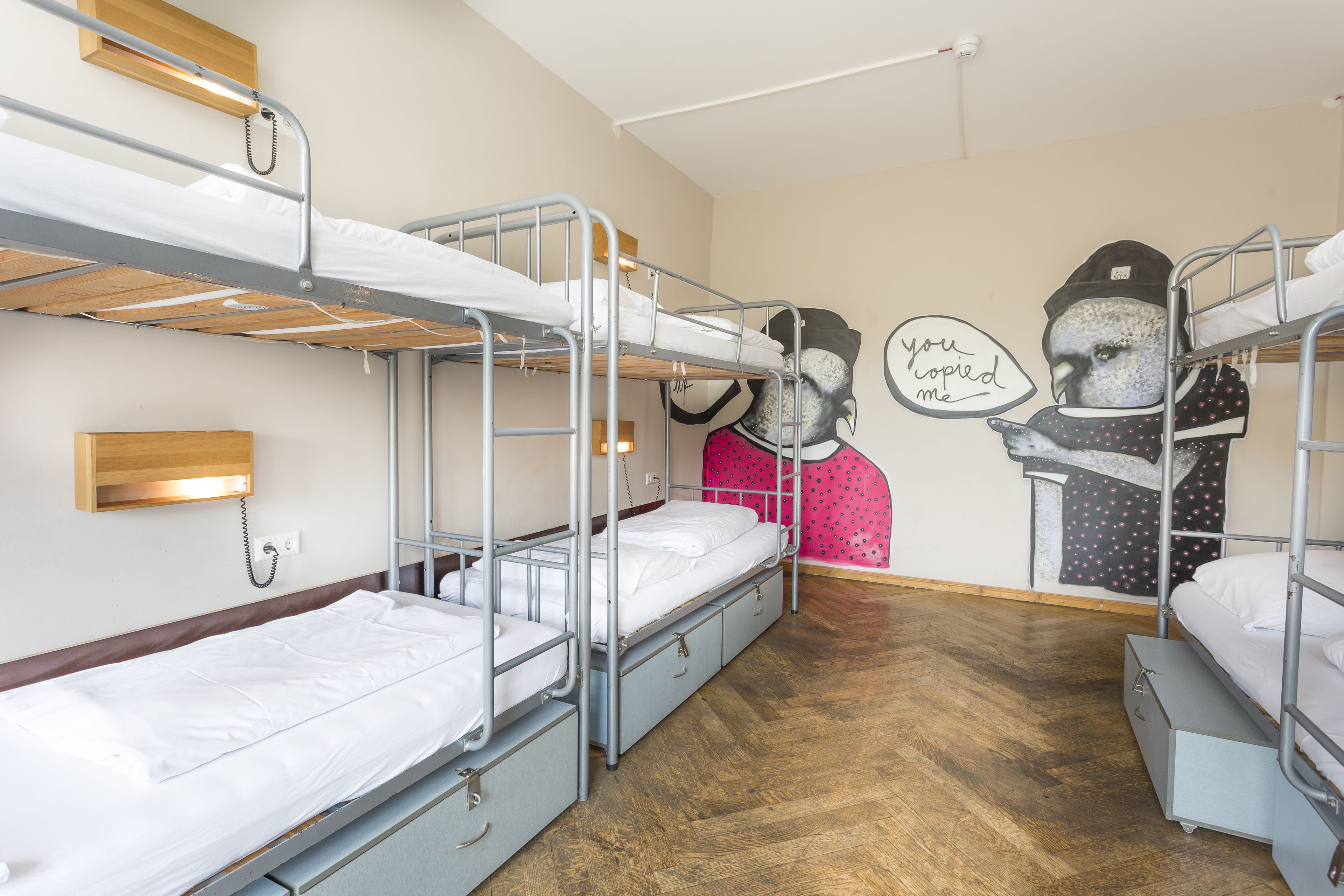 A dormitory room with bunk beds, a wooden headboard, a wall-mounted phone, and a wall decoration.