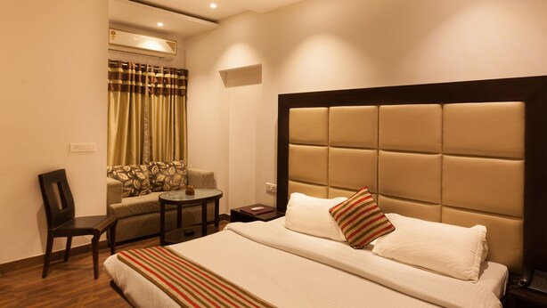 A hotel room with a large bed, a sofa, a small table, and an air conditioning unit. - OYO Rooms Cyber City (Gurugram)
