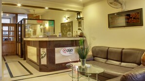 A reception area with a reception desk, a sofa, a glass table, and a fan on the wall. - OYO Rooms Cyber City (Gurugram)