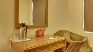 A hotel room with a wooden desk, a mirror, a sofa, and a window with blinds. - OYO Rooms Cyber City (Gurugram)