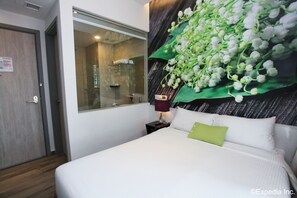Una habitación de hotel con cama, mesita de noche, ventana y zona de ducha.