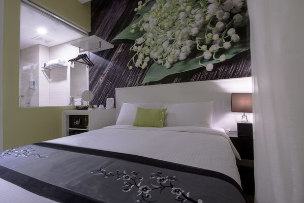 A hotel room with a bed, a bedside table, a lamp, a mirror, and a wall with a floral mural. - J8 Hotel (Singapore)