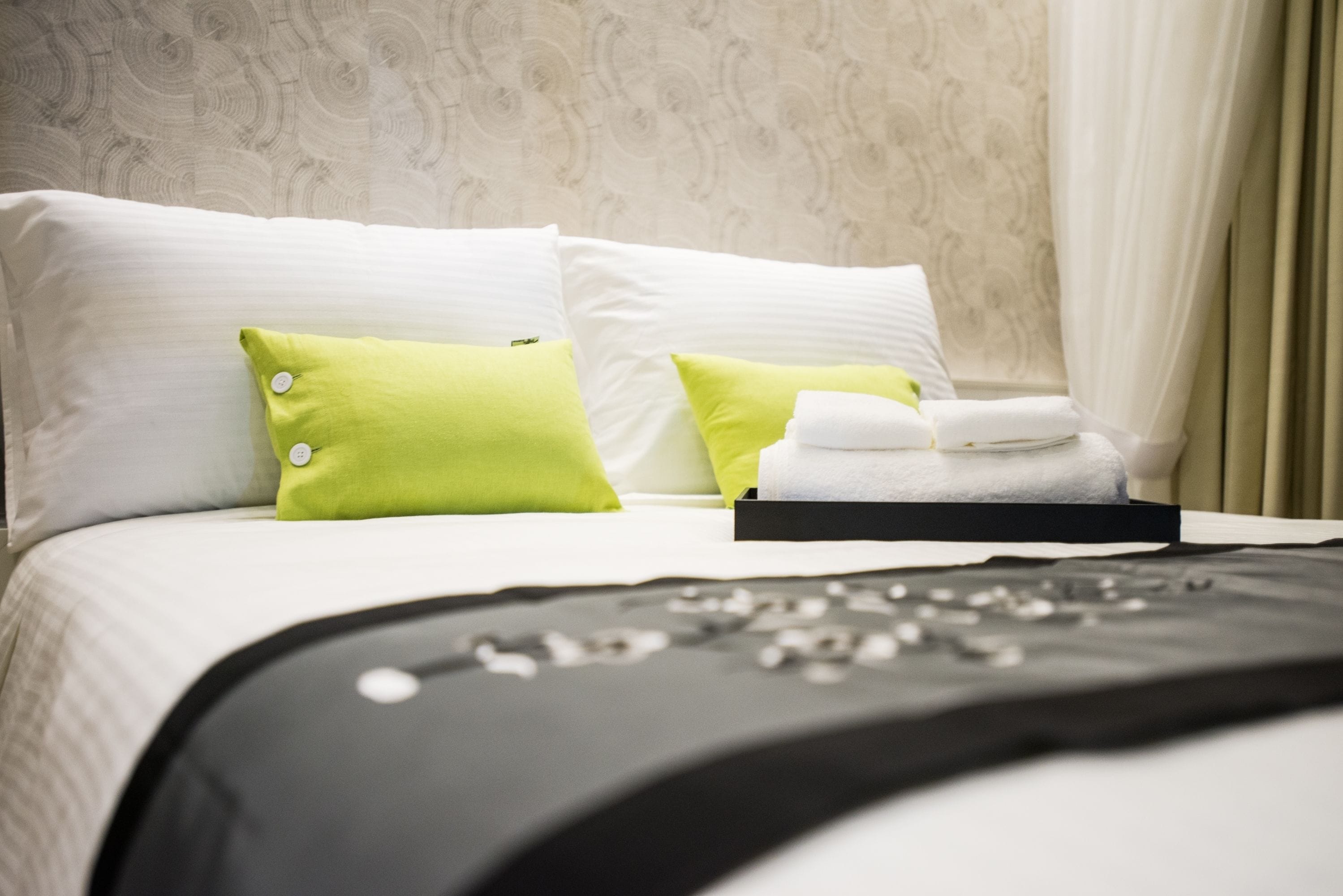 Una cama bien hecha con almohadas blancas y verdes, una manta negra y una toalla doblada.
