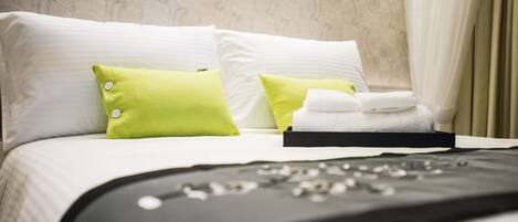 Una cama bien hecha con almohadas blancas y verdes, una manta negra y una toalla doblada.