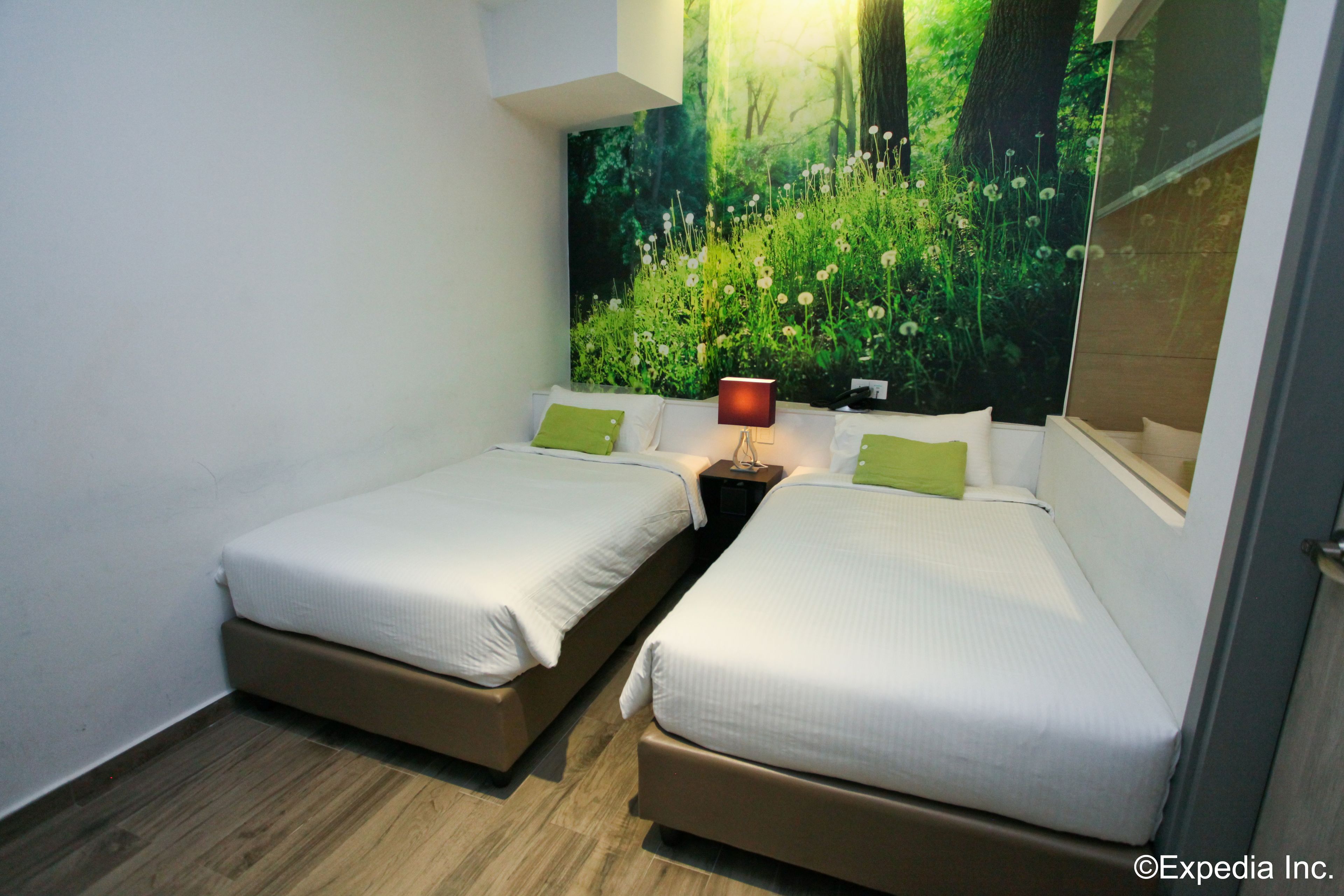 A double room with two beds, a nightstand, a lamp, and a large forest-themed wall mural.