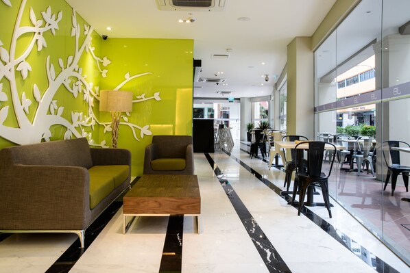 A modern lobby with a green accent wall, a sofa, a coffee table, and a seating area with tables and chairs. - J8 Hotel (Singapore)