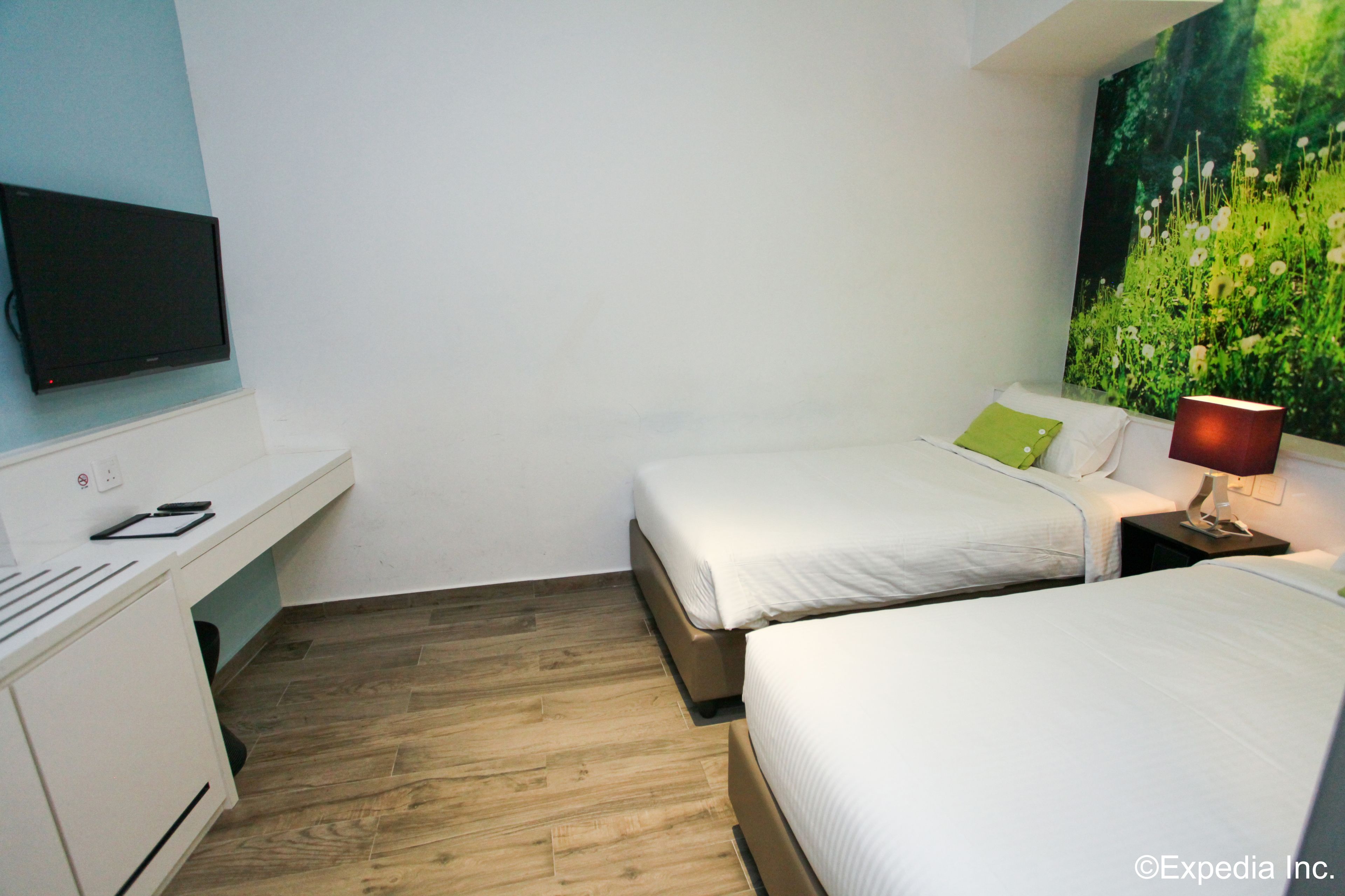 A hotel room with two beds, a desk, a TV, and a painting of a garden.