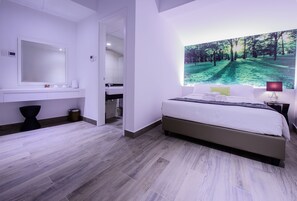 A modern bedroom with a large bed, a bathroom with a mirror, and a wall-mounted TV displaying a forest scene. - J8 Hotel (Singapore)