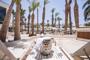 A poolside area with lounge chairs, a table with a drink, and palm trees.