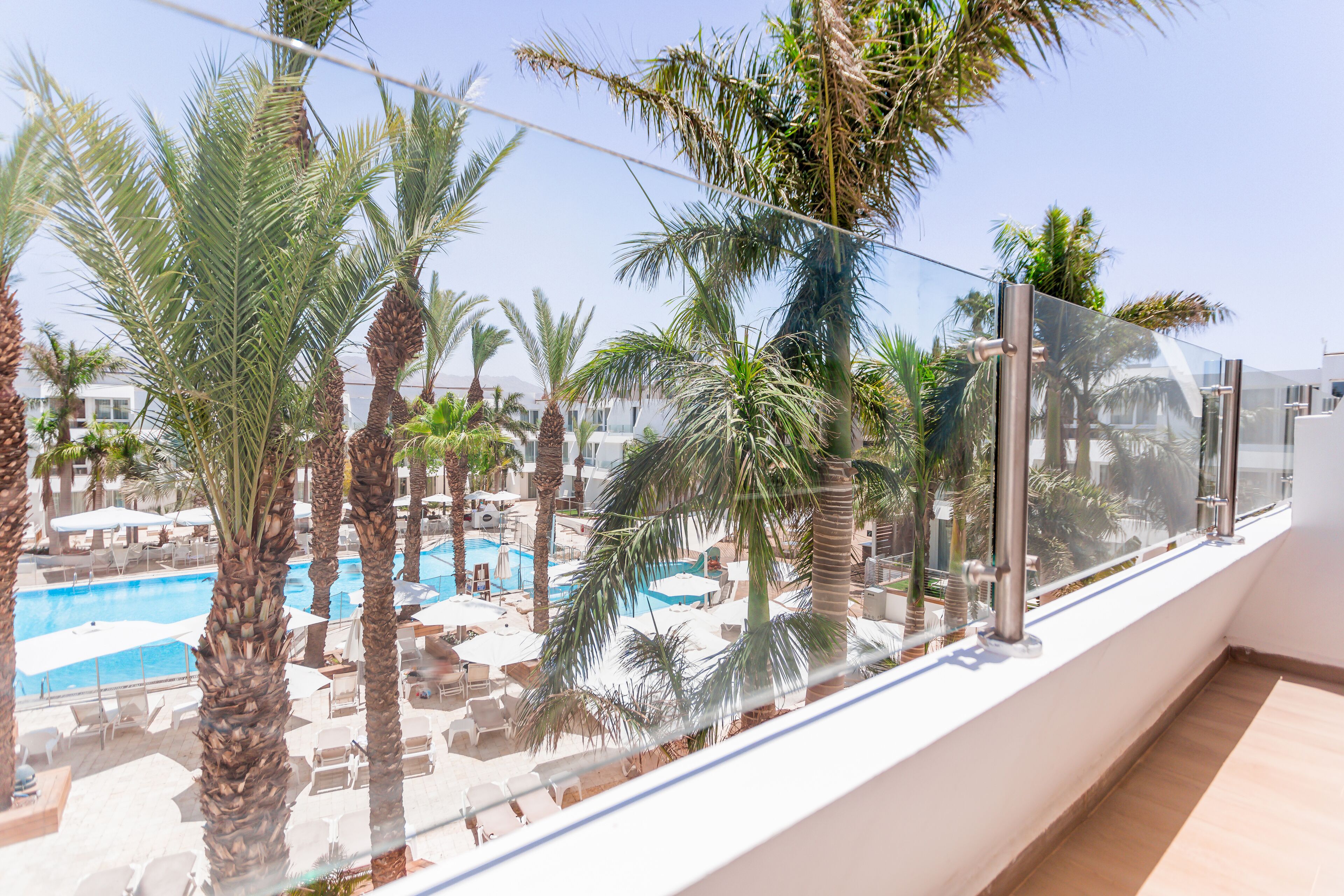 A balcony with a view of a pool area surrounded by palm trees.