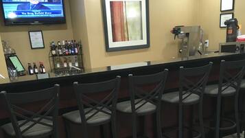 A bar area with a television displaying a news program, a framed artwork, and a coffee machine.